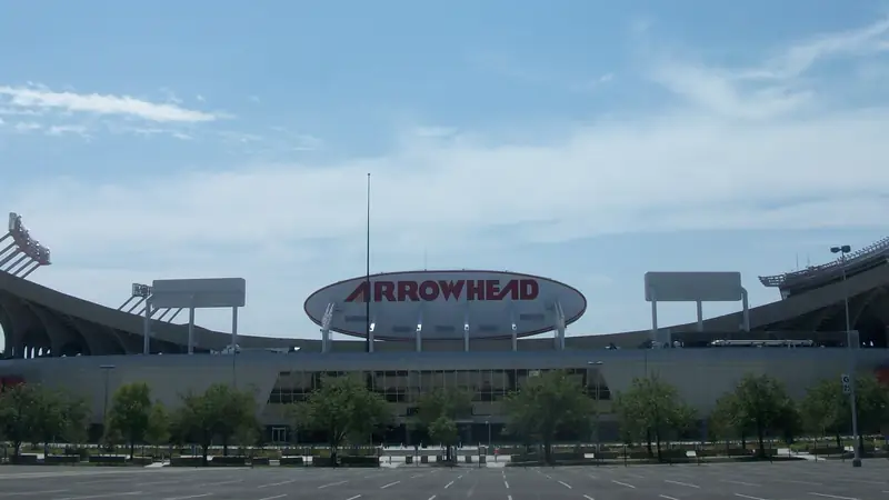 Arrowhead Stadium's exterior and its oval ARROWHEAD sign, seen across the parking lot on a sunny day
