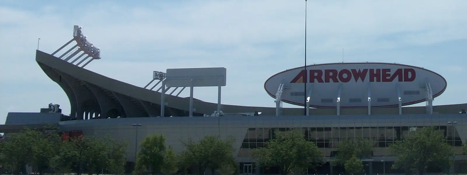 Arrowhead Stadium's exterior and its oval ARROWHEAD sign, seen across the parking lot on a sunny day